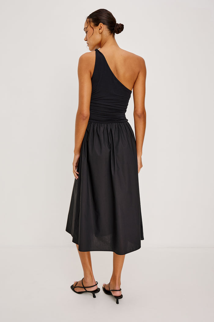 Chayana Midi Dress in Jersey With One-Shoulder Twist Strap Neckline, Waist Shirring, Side Pockets, Poplin Skirt in Black Colorway - Full Body Back View Featured on Model