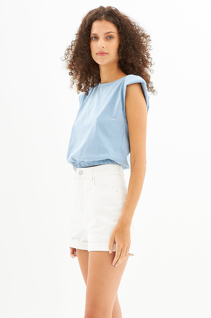 Model wearing Carbon Maya Padded Crop Top in light blue with white denim shorts, featuring an elastic hem.