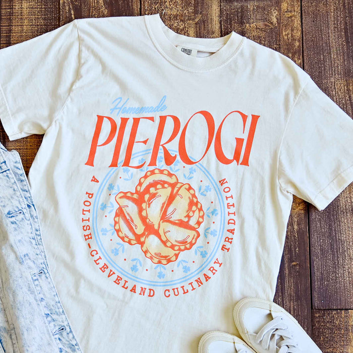 White t-shirt with 'Pierogi' graphic design on a wooden surface