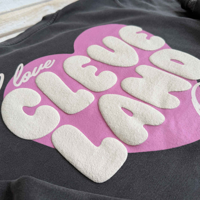 Gray sweatshirt with a pink heart-shaped design featuring white text on a wooden surface.