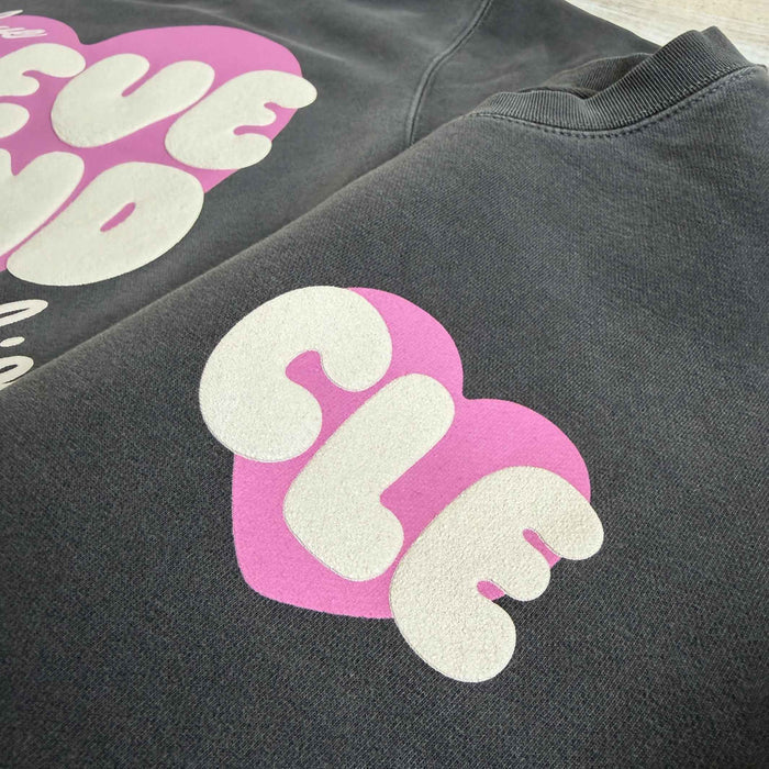 Black sweatshirt with pink and white text design on a flat surface