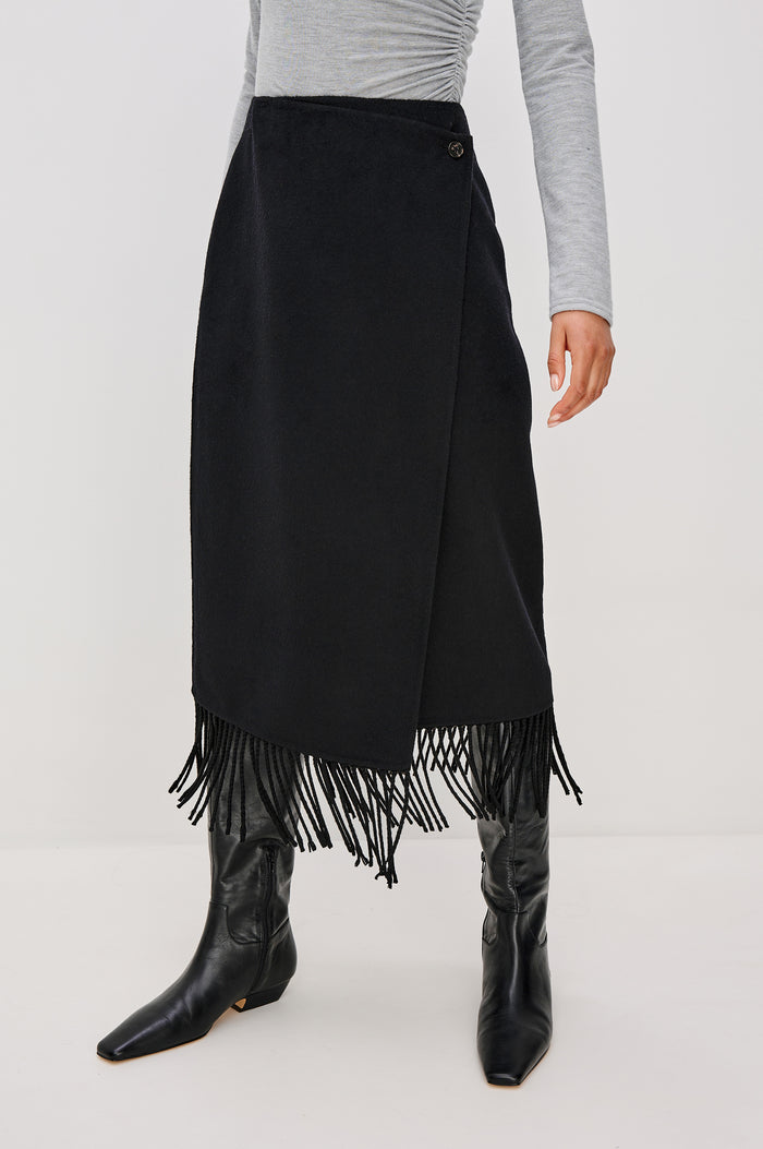 Odette Midi Skirt in Wool Blend With Wrap Design, Hidden Side Button Closure, and Fringe Hem in Black Colorway - Lower Body Front View Featured on Model