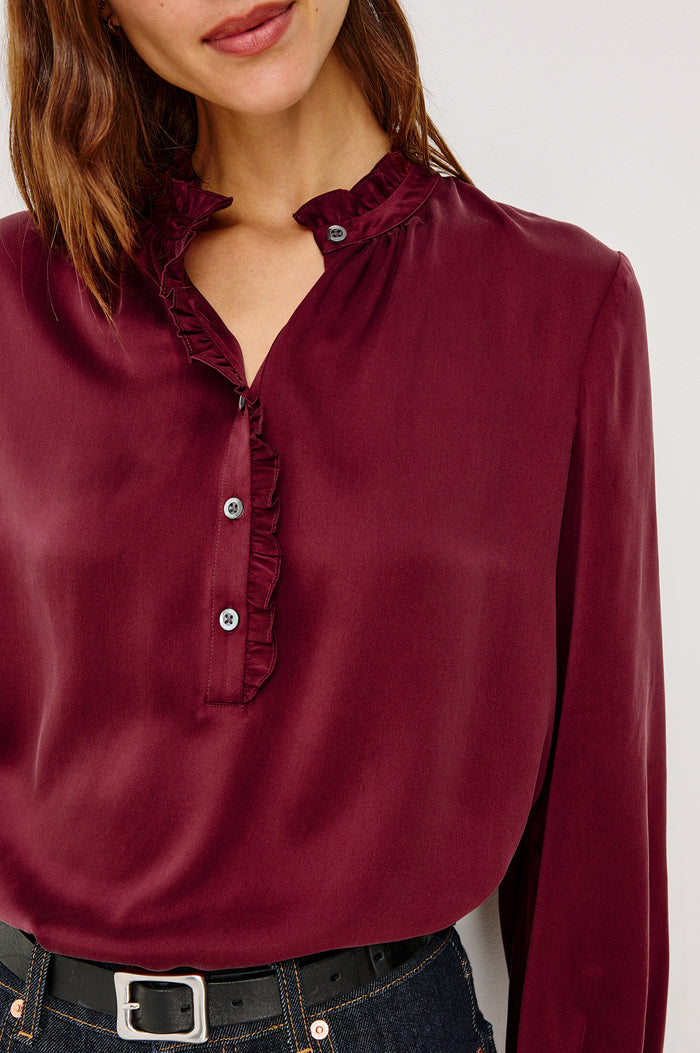 Sien Top in Silk Charmeuse With Ruffled High Neckline, Half Button Placket, and Long Billowing Sleeves With Fitted Cuffs in Garnet Colorway - Upper Body Close Up Front View Featured on Model